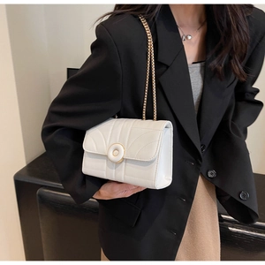 Detail of white quilted crossbody bag with wave texture and round gold buckle