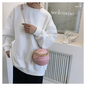 Detail of a pink basketball-shaped crossbody bag with gold chain and printed letters