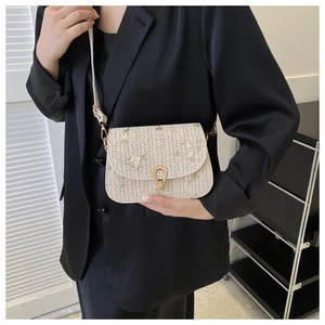Detail of floral embroidery and gold U-shaped buckle on a straw crossbody saddle bag
