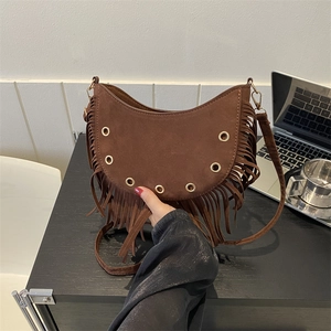 Brown suede crescent bag with fringe details and metal eyelets on a desk