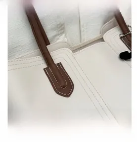 Dettaglio ravvicinato della borsa beige con manico marrone e cuciture bianche a vista