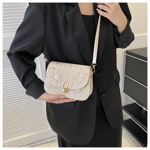 Detailed view of straw saddle bag featuring floral embroidery and horseshoe gold buckle
