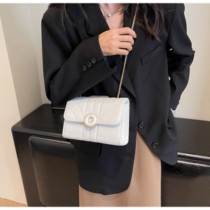 Close-up of a white quilted shoulder bag with a gold buckle on a model's outfit