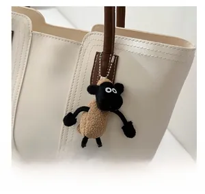 Dettaglio di un ciondolo a forma di pecora in peluche sul manico di una borsa in pelle beige