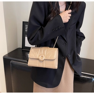 Model wearing a minimalist cream chain crossbody bag with quilted texture and gold ring buckle