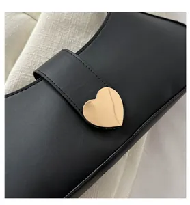 Detailed view of the gold heart-shaped metal buckle on a black minimalist PU leather handbag