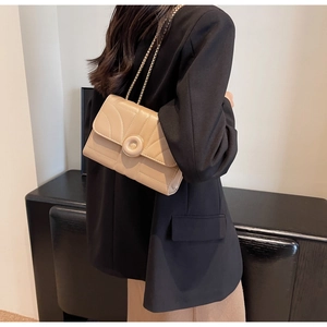 Model wearing a beige quilted chain crossbody bag with a round gold buckle detail