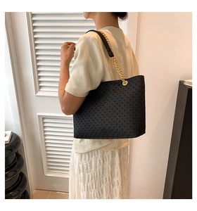 Detalle del bolso tote tejido negro con correa de cuero y cadena dorada en modelo