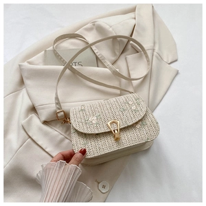 Detail of floral embroidery and gold metal buckle on a beige woven straw saddle bag