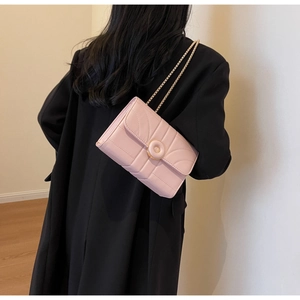 Detail of pink quilted leather crossbody bag with metal chain strap on black coat