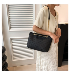 Detalle de bolso tote negro tejido con cadena dorada lucido por una modelo con estilo