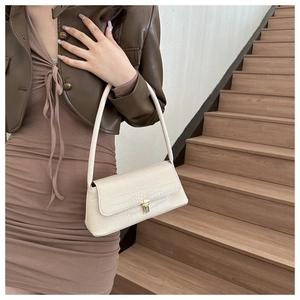Close-up of beige faux crocodile leather texture and golden metal lock on baguette bag