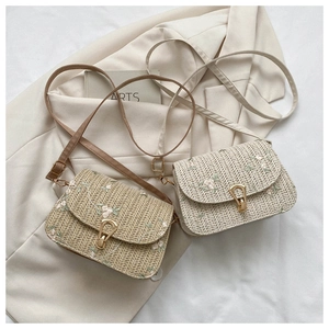 Straw crossbody bag with floral embroidery and gold buckle on a beige blazer background