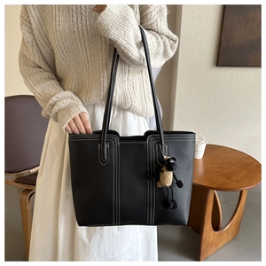 Dettaglio borsa shopper nera con cuciture a contrasto e ciondolo a pecora su un maglione