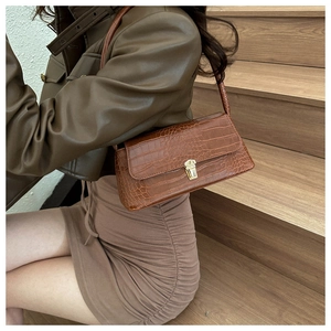 Close-up of brown crocodile texture shoulder bag with gold metal clasp on a leather jacket