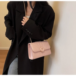 Close-up of pink quilted crossbody bag with gold chain strap on a black blazer