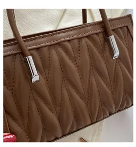 Detail of brown leather bag with V-shaped quilting and silver metal handle accents