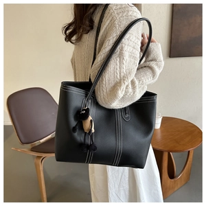 Dettaglio della borsa tote in pelle nera con cuciture bianche e ciondolo a forma di pecora