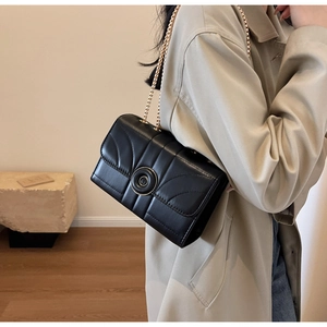 Detailed view of a black quilted crossbody bag with a gold chain strap and round lock
