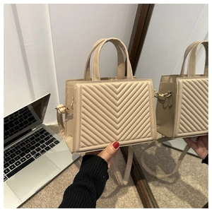 Detail view of beige tote bag featuring V-shaped quilted texture and gold hardware