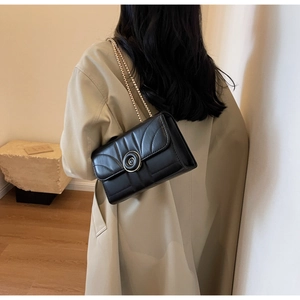 Detail of black quilted shoulder bag with golden chain strap and round metal buckle