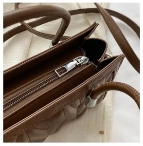 Close-up of smooth silver zipper and quilted leather texture on brown crossbody bag