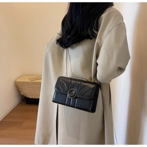 Close-up of black quilted shoulder bag with gold chain and circular swivel lock details