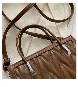 Detail of wave quilted brown faux leather handbag with silver cylindrical hardware and strap