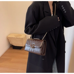 Detail of dark brown quilted leather crossbody bag with a vintage round metal buckle