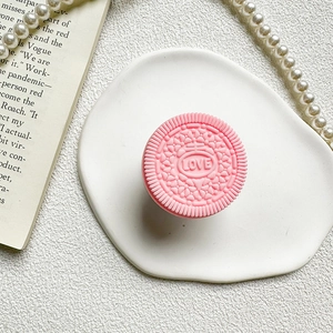 Detail of pink biscuit shaped phone grip with LOVE engraving on a white ceramic tray