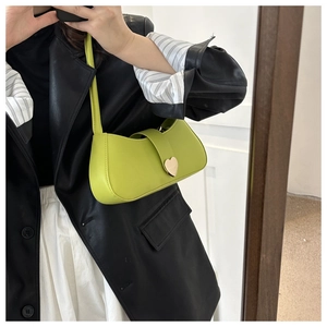 Detail of lime green baguette bag with golden heart clasp on model's shoulder