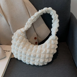 White popcorn textured crescent shoulder bag placed on a grey sofa with magazines