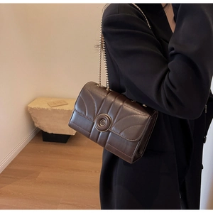 Detail of a dark brown quilted shoulder bag with gold chain and circular metal clasp