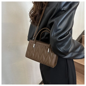 Detail of a brown quilted handbag with V-shaped stitching and adjustable strap on a model