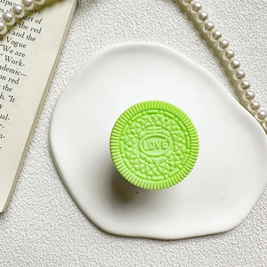 Macro shot of a mint green cookie-shaped phone grip with LOVE text on a ceramic tray