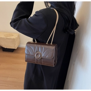 Detail of dark brown quilted crossbody bag featuring gold chain strap and magnetic closure