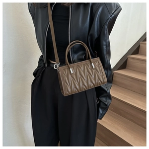 Detail view of brown matelassé pleated handbag with twin handles and silver hardware