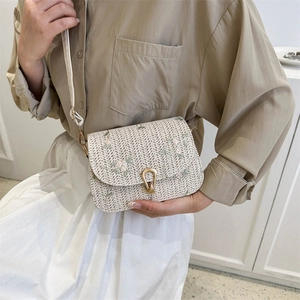 Floral embroidered straw saddle bag with gold horseshoe buckle on woman shoulder