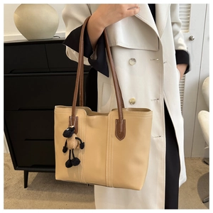 Dettaglio della borsa tote beige con manici marroni e ciondolo a pecora su modella