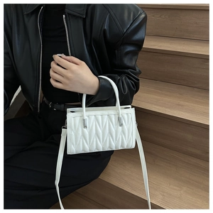 White quilted handbag with V-shaped texture and silver hardware shown with black leather jacket