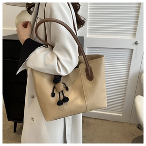 Dettaglio di borsa tote beige in finta pelle con tracolla marrone e ciondolo a pecora