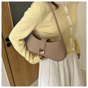 Detail of minimalist solid color underarm bag with gold heart clasp on a female model