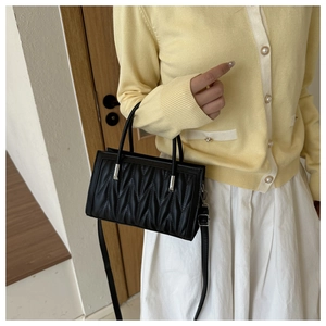 Detail of black quilted shoulder bag with V-shaped stitching and silver metal hardware