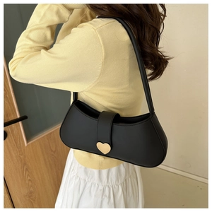 Detail of black underarm bag with gold heart buckle worn by model on shoulder