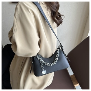 Detail of black leather crescent bag with silver chain and metal charm on a beige coat