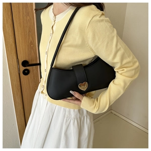 Close-up of minimalist black leather underarm bag with gold heart-shaped buckle on model