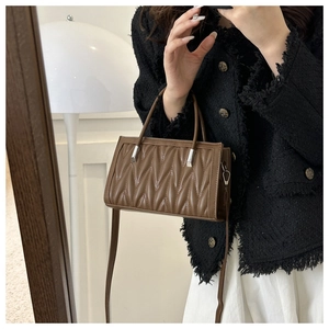 Close-up of brown quilted leather handbag featuring V-shaped texture and metal handles