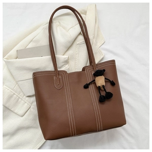 Dettaglio di una borsa tote marrone con cuciture bianche a contrasto e ciondolo a forma di orso