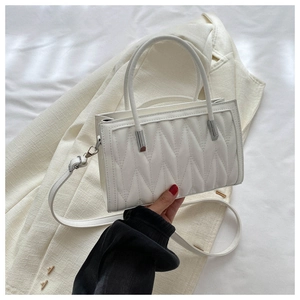 Detail of white quilted handbag featuring elegant wavy stitching and cylinder handles