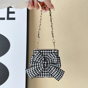 Detail of houndstooth flip phone case with decorative bow and woven metal chain strap